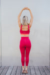 La coach sportive Julie Pujols posant debout avec les mains pointées en haut, de dos. Elle porte la tenue azar gang couleur framboise.