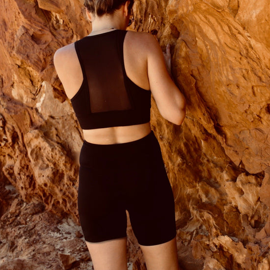 femme debout, de dos, contre des roches, portant une tenue de sport noire de la marque AZAR GANG