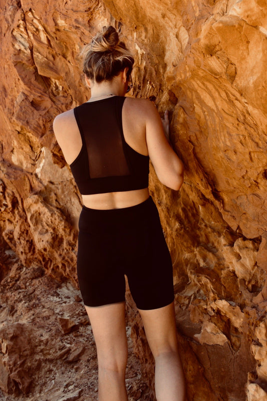 femme debout, de dos, contre des roches, portant une tenue de sport noire de la marque AZAR GANG
